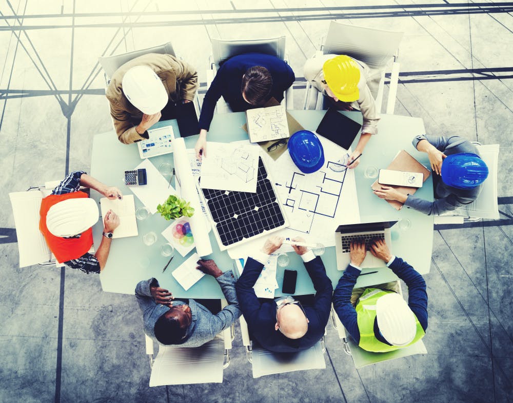 Overhead shot of eight construction workers sitting at a desk looking at drawings