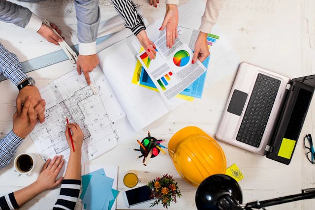 Over head shot of employees looking at drawings and charts solutions PC header 1200x800