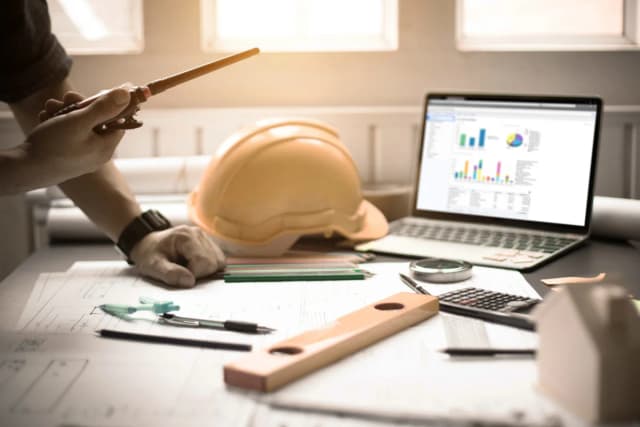 Yellow construction helmet on desk with laptop with graphs on it - 1200x800