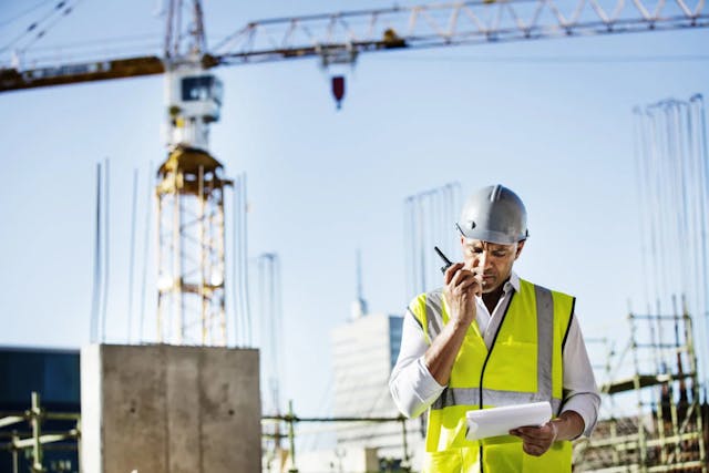 Construction worker on a walkie talkie with a crane in the background 1200x800