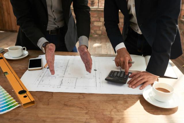 Two executives looking at a drawing and using a calculator on a table