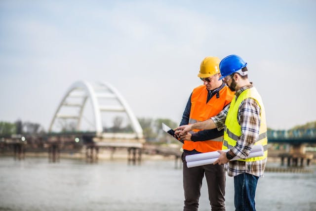 Two construction workers at a work site looking at an iPad 1200x801