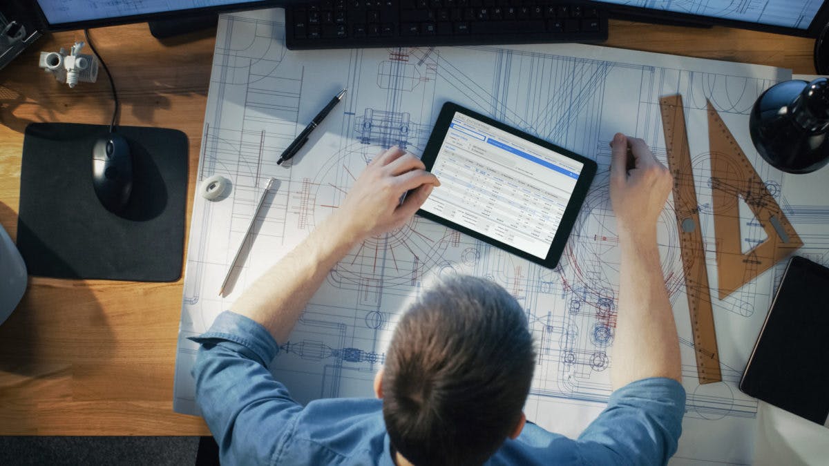Over head shot of construction worker looking at an iPad and drawings 1200x675