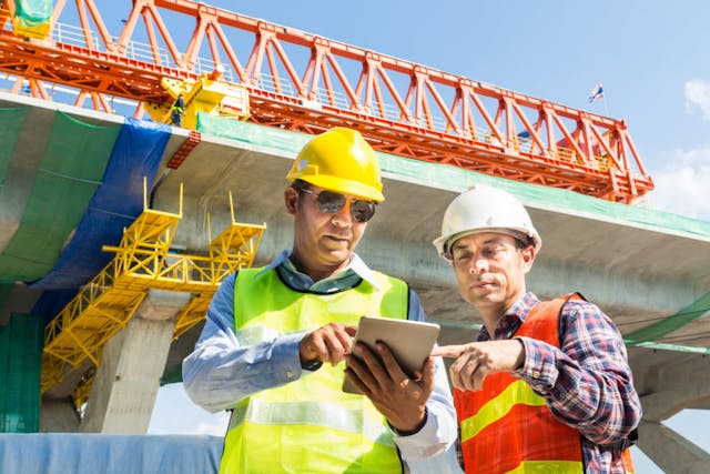Two construction workers looking at an iPad infront of a crane 1200x800