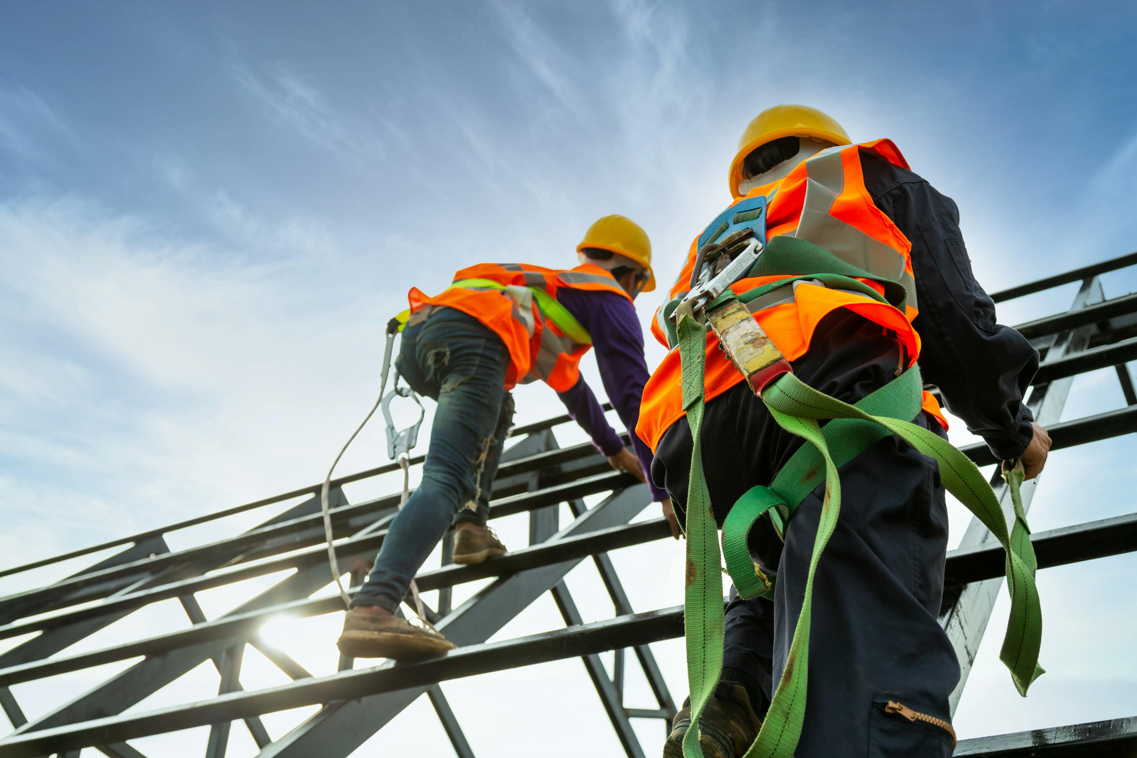 Two construction workers climbing beams