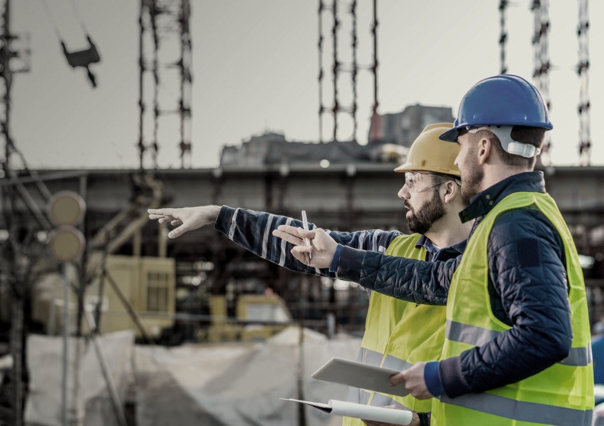 Two male construction workers at a site pointing 1200x847