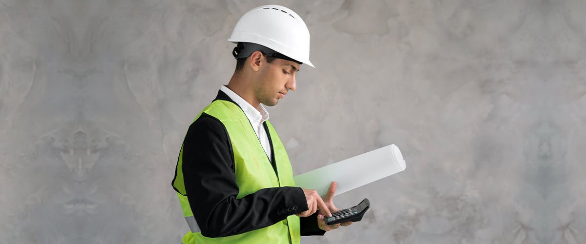 Male construction working holding rolled drawings and using a calculator